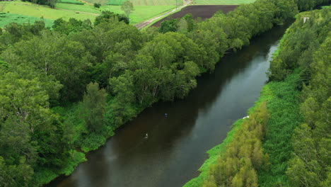 Aerial-4K-Drone-Flyover-Of-Fisherman-Walking-In-Creek-Surrounded-By-Green-Bush-In-Australia