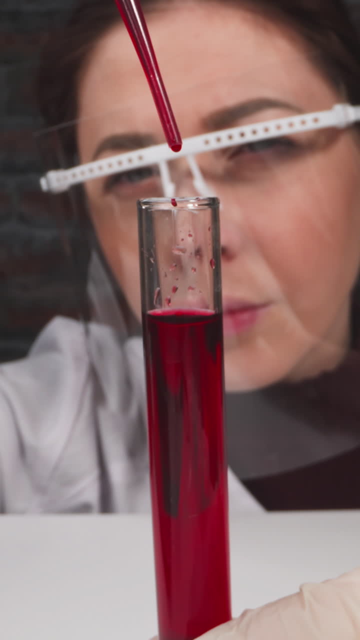 Asian woman scientist with protective goggles drips catalyzer into test tube with liquid in clinic slow motion. Probe lens shot of vaccine closeup