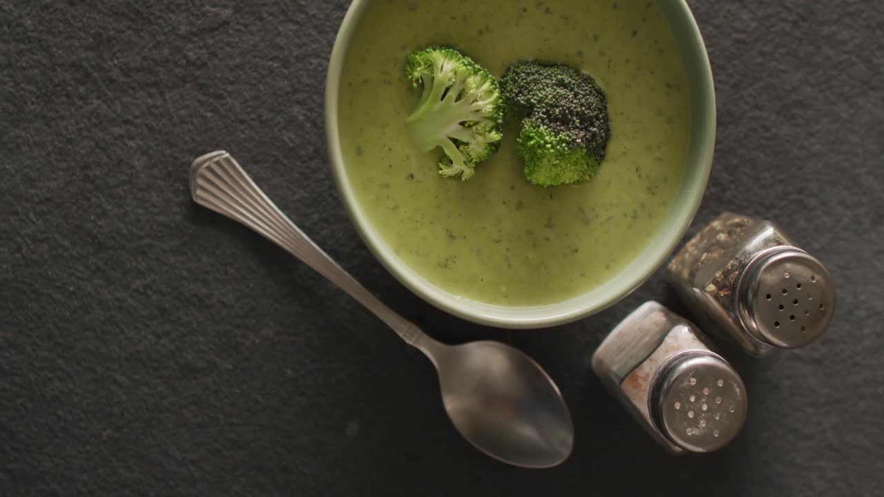 Video of cream broccoli soup in bowl on grey table with spoon and spices