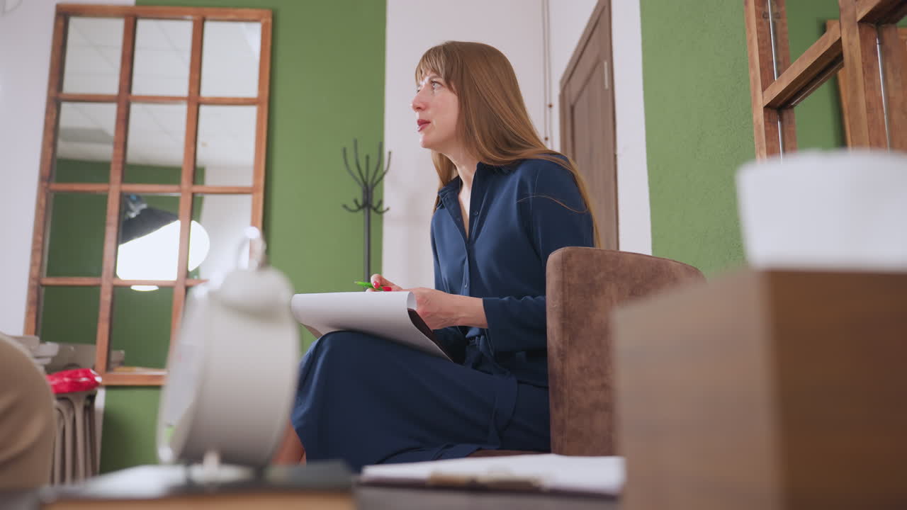 Focused wellness guide writes on notepad with passion in her eyes while lifting head to engage warmly with visitor in peaceful therapeutic environment, expressing understanding through conversation