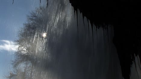 Shot-from-behind-a-waterfall-with-the-sun-appearing-behind-the-water-in-Edessa,-Greece