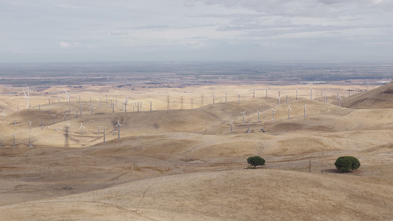 amplia toma de colinas secas y molinos de viento en un día nublado como molinos de viento lejanos giran