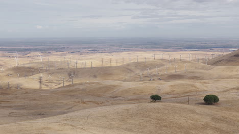 Wide-shot-of-dry-hills-and-windmills-on-cloudy-day-as-distant-windmills-turn