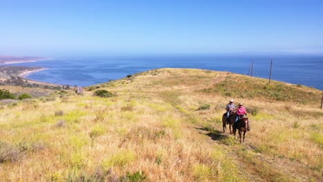 Antena-Pareja-De-Jubilados-A-Caballo-En-La-Cima-De-La-Montaña-Con-Vistas-Al-Océano-O-La-Costa-En-Un-Rancho-Cerca-De-Santa-Barbara,-California