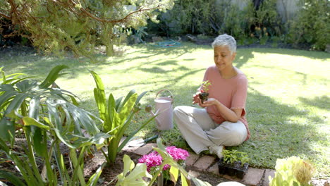 Feliz-Mujer-Birracial-Mayor-Plantando-Plantas-En-Un-Jardín-Soleado-En-Casa,-Cámara-Lenta