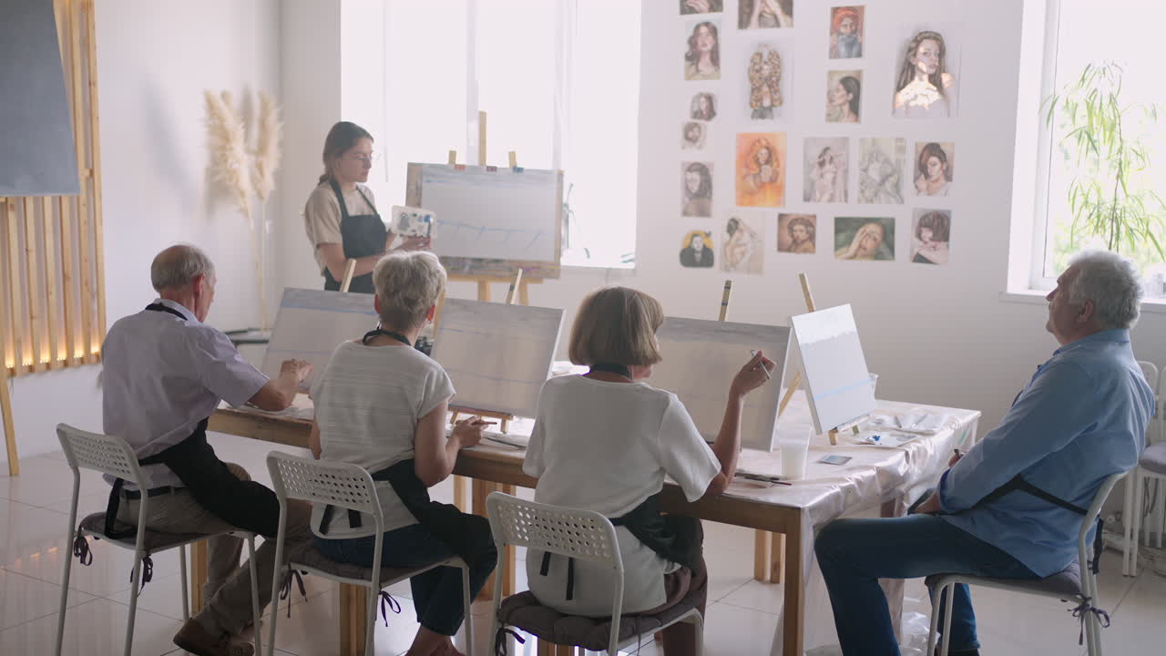 vista de ángulo alto de amigos mayores alegres pintando en lienzo. mujer mayor sonriendo mientras dibuja con el grupo. mayores asistiendo a clase de pintura juntos. hombres mayores divirtiéndose pintando en clase de arte