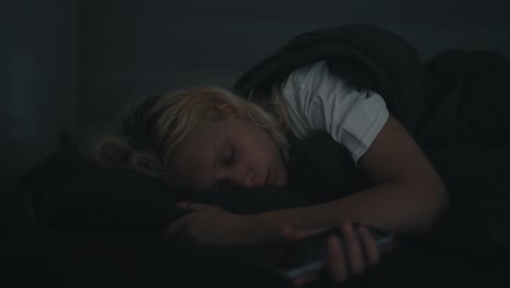 a blonde girl in a white t-shirt wakes up abruptly and looks anxiously at the phone at night