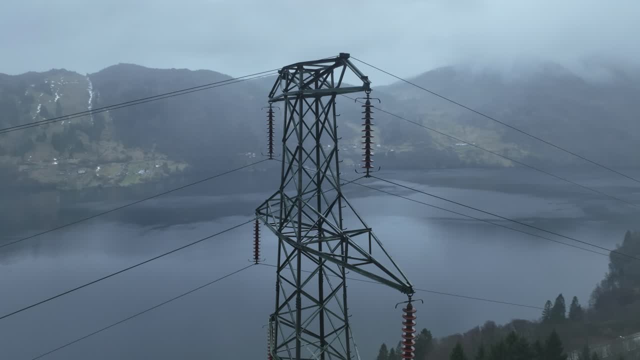 High voltage powerline mast in Romslo Norway, with a view over Sorfjorden towards Osteroy island. Rainy, moody atmosphere with fog and parallax effect