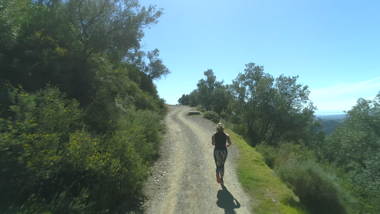 Mujer corriendo cuesta arriba en un hermoso paisaje en un día soleado con cielo azul despejado.