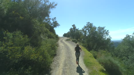 Woman-running-uphill-in-a-beautiful-landscape-on-sunny-day-with-clear-blue-sky