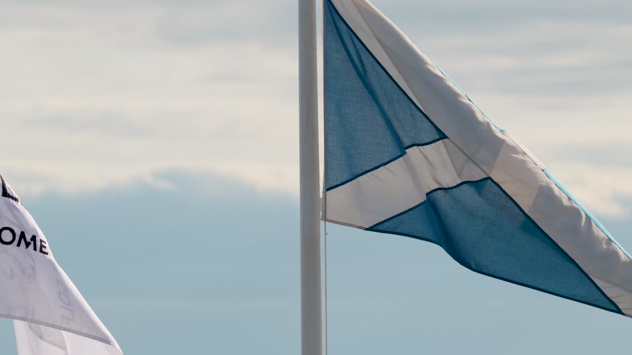 To flag vejer i dagslysbrisen, blå himmel i baggrunden, medium telefotopejling, jævn kamerapanorering