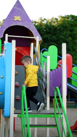 kid in yellow jumper and black pants goes up the stairs of the slide. baby boy moves into the tube slide on the playground. vertical video.