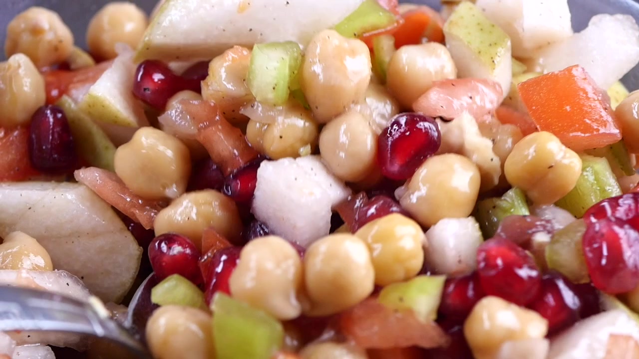 Taze nohut ve nar salatasını karıştıran bir kaşığın yakın çekimi.