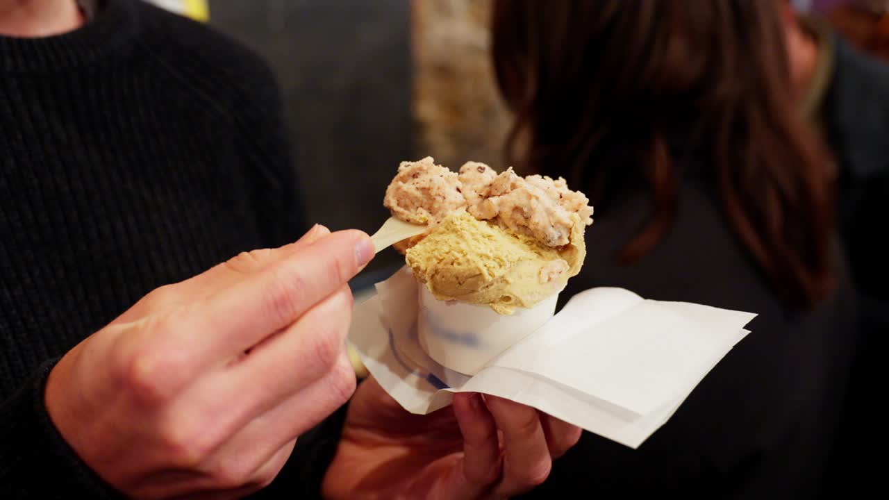 A person holding an ice cream cone topped with a large scoop, with a toothpick in their hand