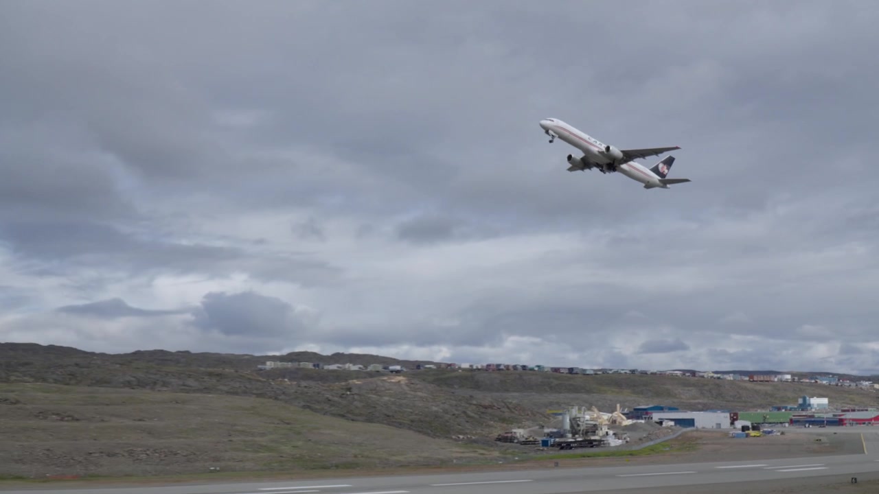 Dynamisk tele-tracking-skud af et kommercielt fragtfly, der accelererer ned ad startbanen og stiger stejlt op i overskyet himmel over Iqaluit