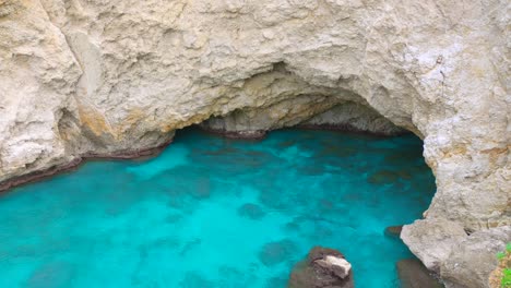 sea cave in sicily with crystal-clear turquoise water, surrounded by rugged limestone cliffs and submerged rocks beneath surface. high angle shot