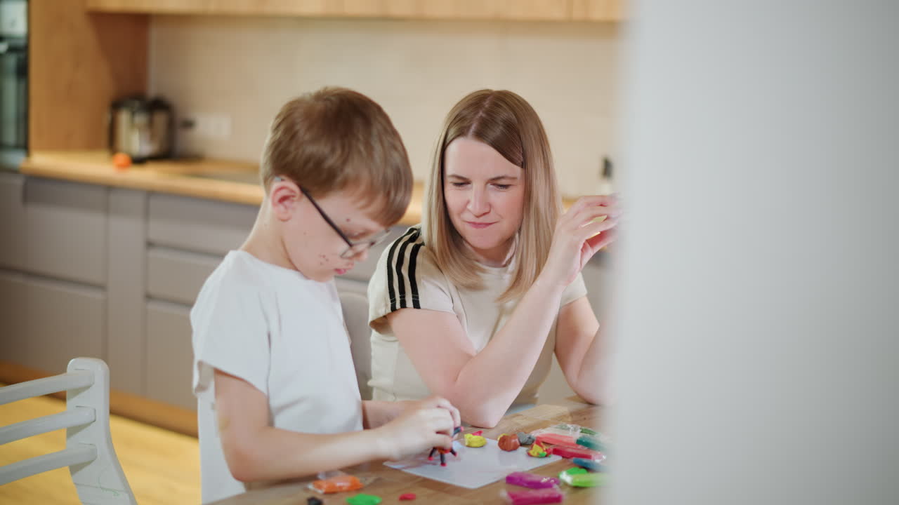 Mother and son sitting together at wooden table near aquarium, engaging in creative play with colorful modeling clay, sharing quality bonding time in cozy home kitchen with fun and learning atmosphere