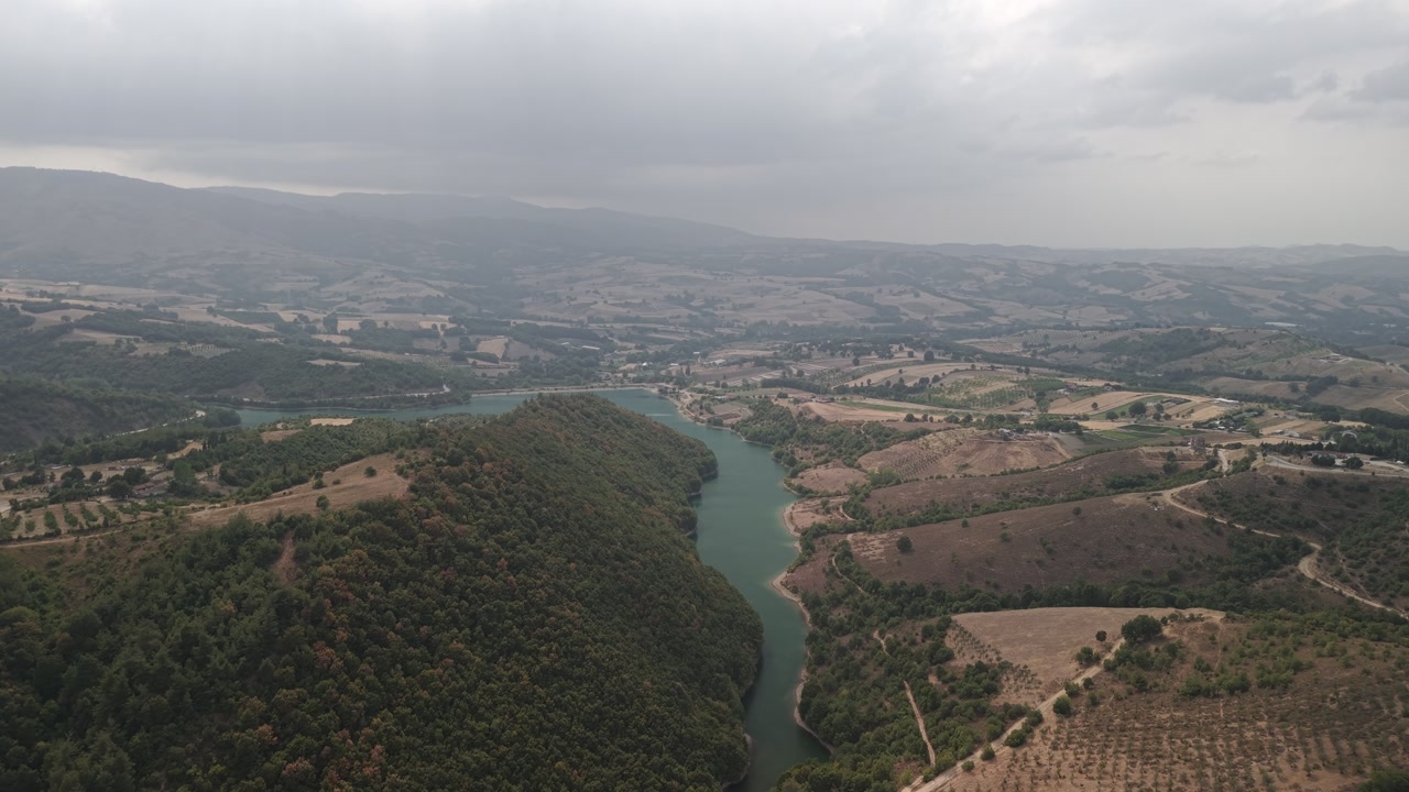 Aerial drone forward shot over the Yalakdere River flowing through green countryside and farmland in Gölcük, Kocaeli, Turkey on a cloudy day.