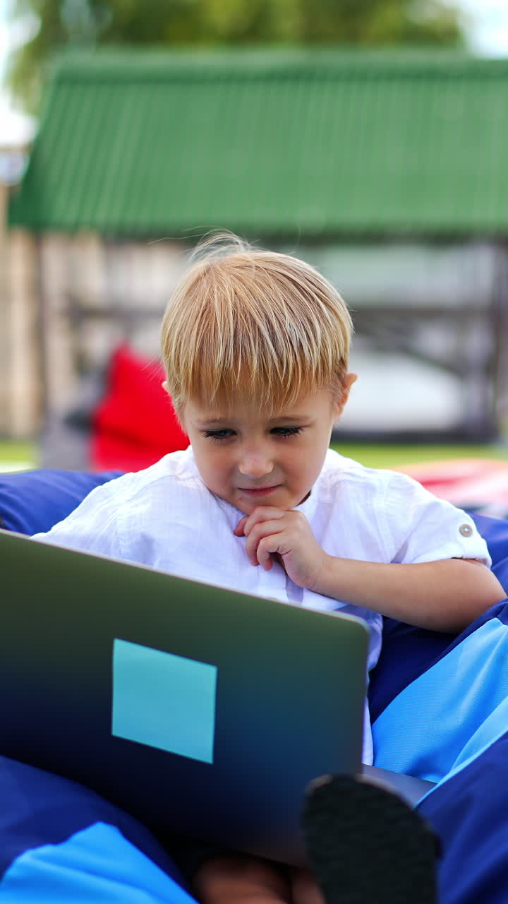Cute boy sitting outdoor with laptop. Small kid learning outdoor with computer. Vertical video