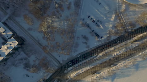 Aerial-drone-shot-flying-directly-over-a-large-highway-travelling-through-an-urban-city-covered-in-sparkling-white-snow-during-winter