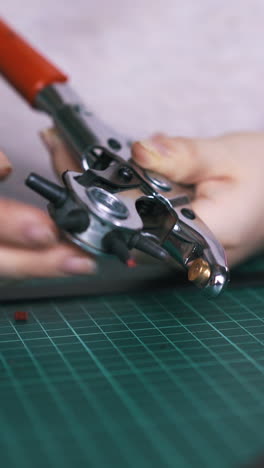cu: professional designer prepares leather belt hole punch pliers on green cutting board in workshop close view