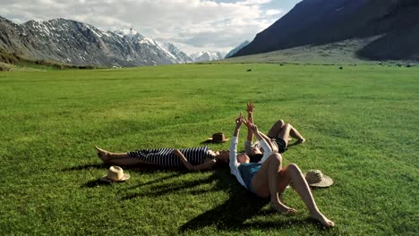 tres chicas atractivas acostadas en la hierba verde y divirtiéndose en un prado día soleado y fondo de montaña