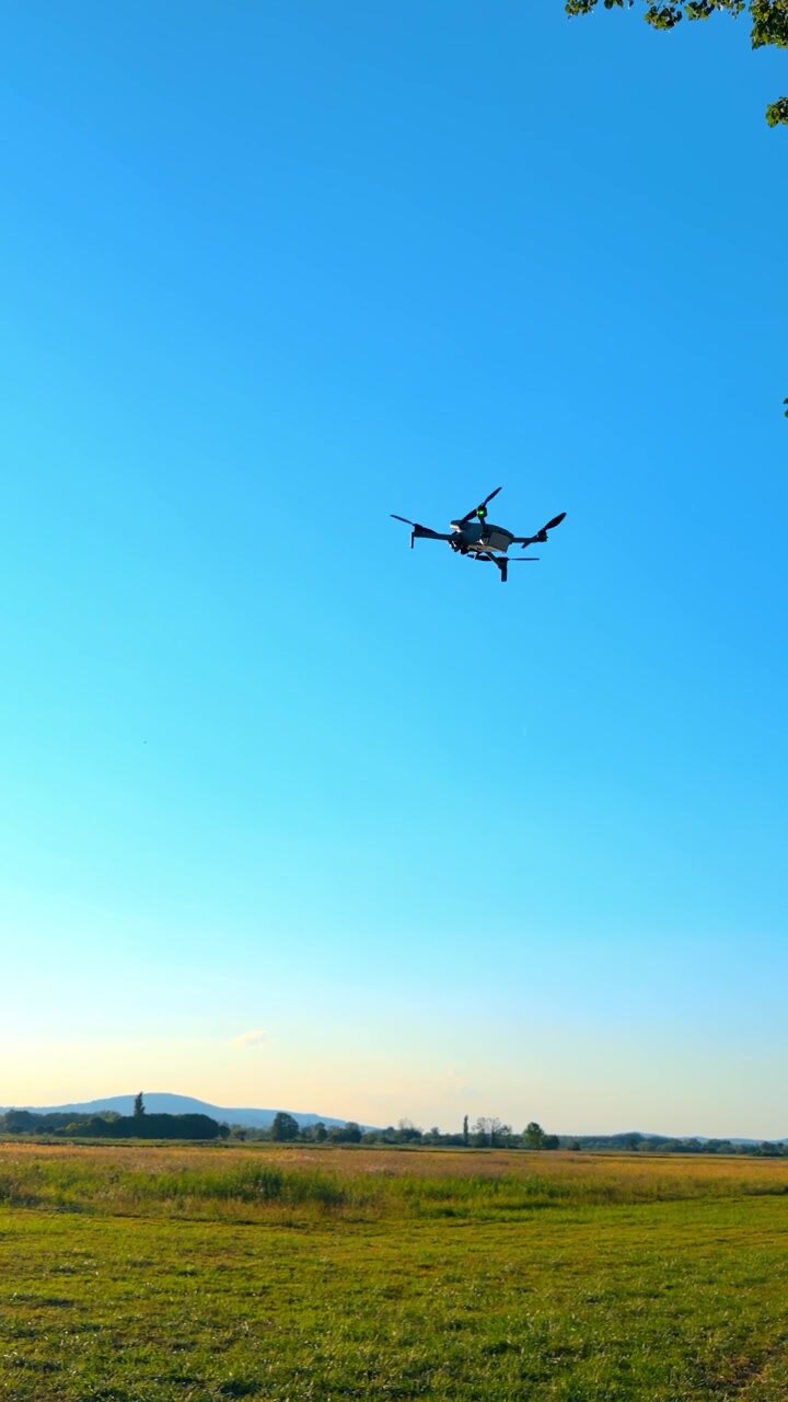 Fjernstyret quadcopter-drone flyver over et grønt landskab. Et ubemandet luftfartøj flyver på en klar blå himmel over åbne landlige marker