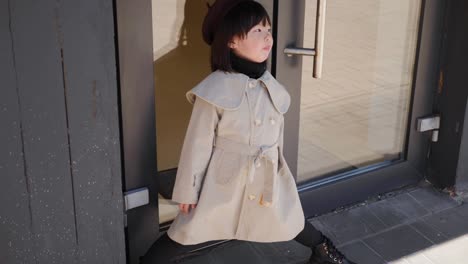 korean girl in a gray coat and cap stands the street in spring at the glass doors of the store