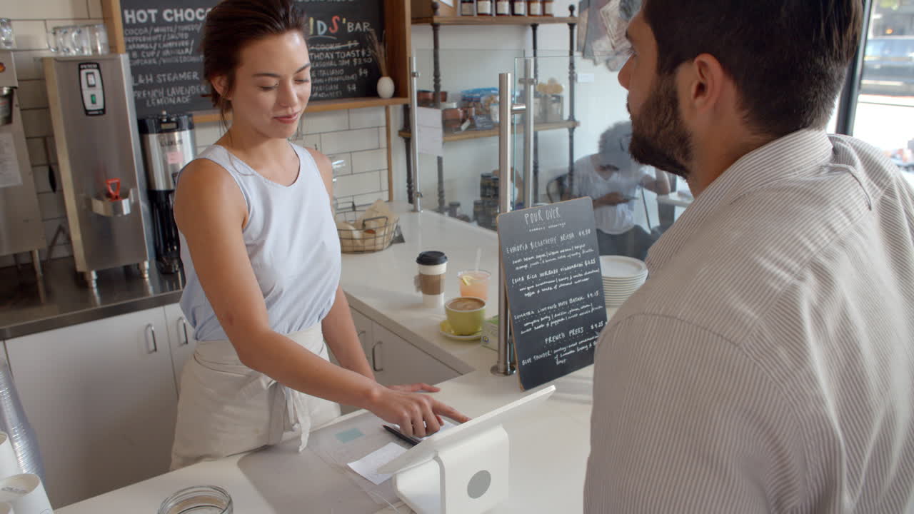 el cliente de la cafetería paga a la camarera sonriente con una tarjeta.