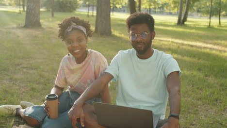 portrait of positive african american man and woman sitting on grass in park