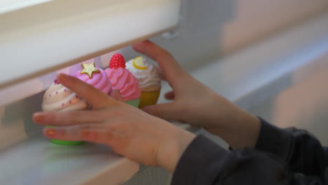 kid playing and putting beautiful decorated cup cakes in front of the window