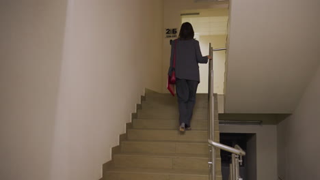 businesswoman walking upstairs in office building carrying red leather handbag, focused and confident. stylish and professional in office attire, heading to work with determination and focus