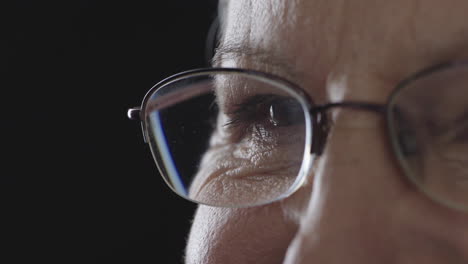 close up of old woman eye blinking wearing glasses isolated on black background copy space