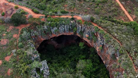 aerial drone lowering shot of the large lapa doce cave entrance of colorful rocks with a self-contained rainforest below in the chapada diamantina national park in bahia, northeastern brazil