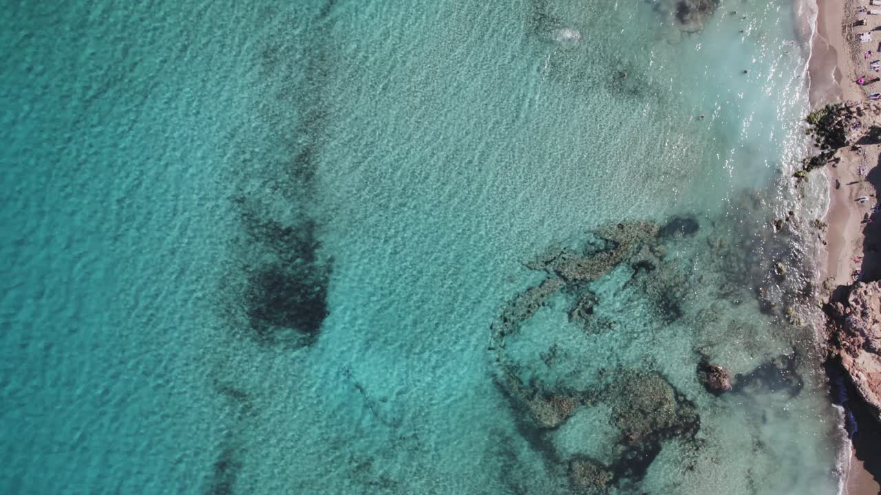topshot del agua azul en la playa con arena y algunas piedras