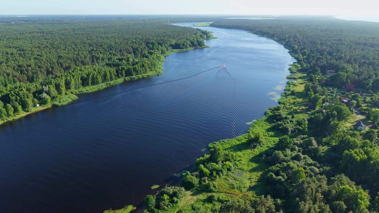 Il drone gira a sinistra mentre una barca lascia una scia lungo il tranquillo fiume Bullupe vicino a Riga.
