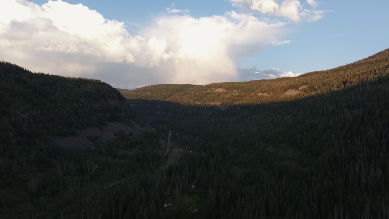 Drone dolly in wide shot of the Uinta-Wasatch-Cache National Forest in Utah during a summer sunset, showing Highway 150, pine trees, Provo River, and Bald Mountain rising above the valley