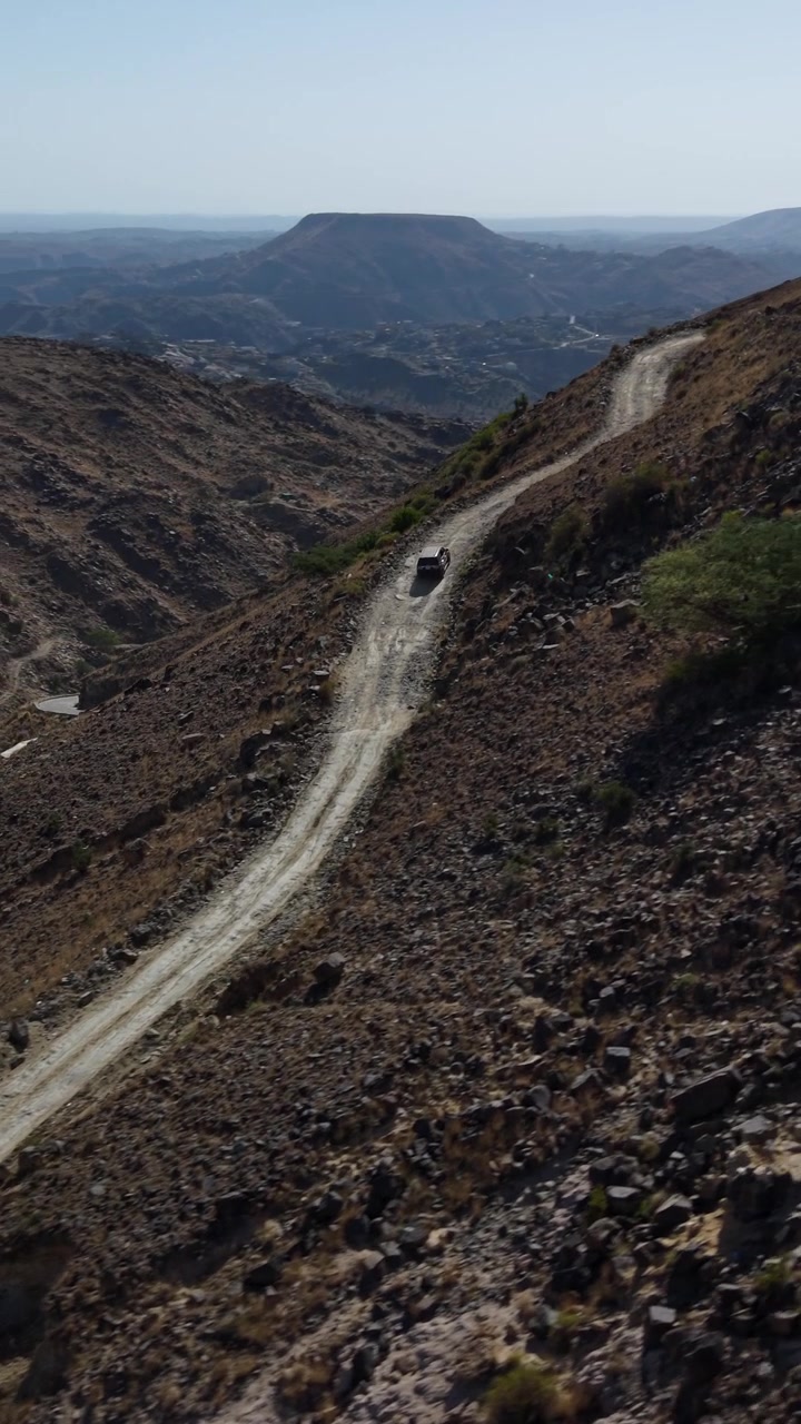Off-road vehicle maneuvering along a perilous winding dirt road in the remote yafa'a mountains of yemen.
