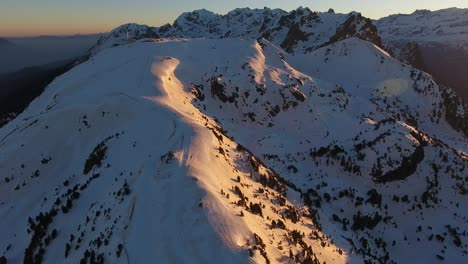 Snow-capped-summit-of-Chamrousse-ski-resort-in-the-French-Alps-early-sunrise,-Aerial-orbit-around-shot