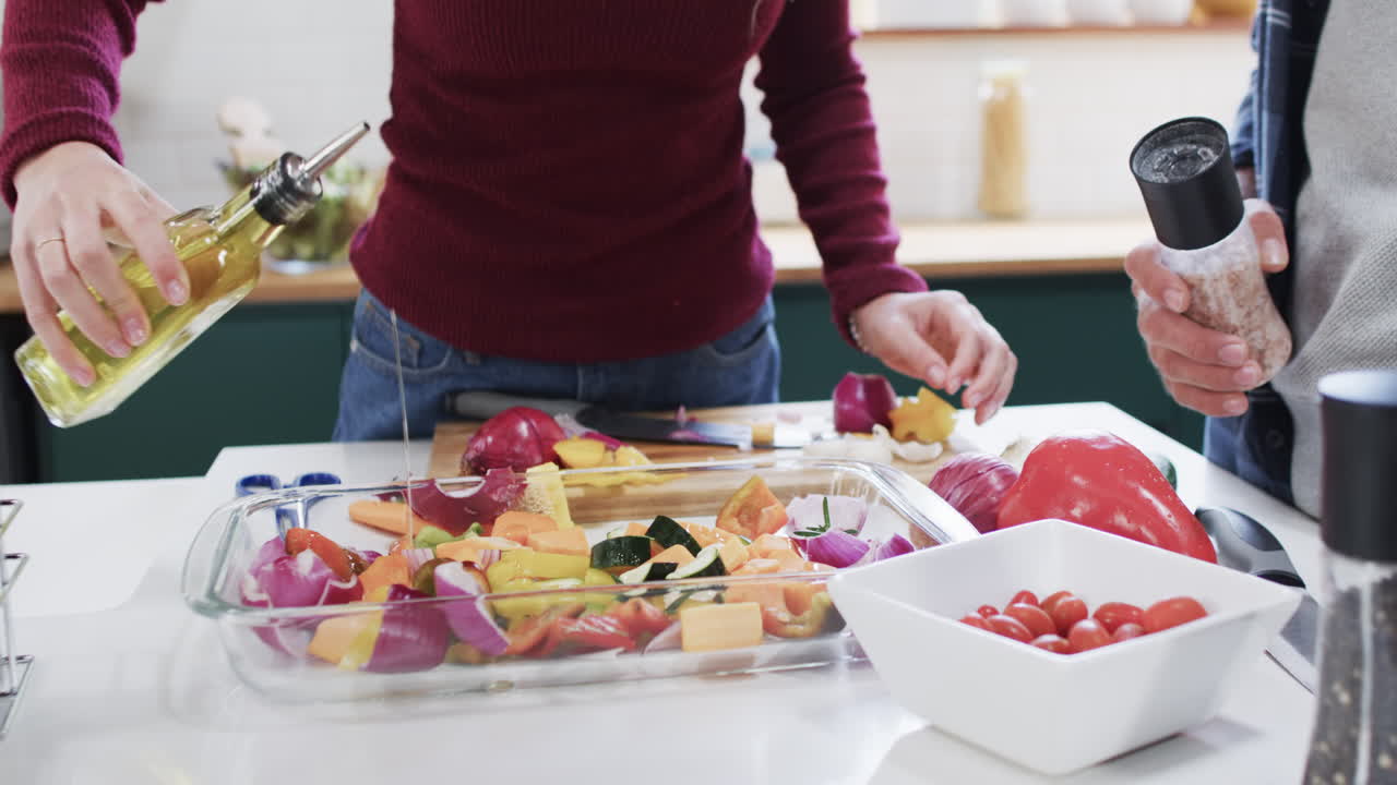 sección media de una pareja diversa preparando la cena en la cocina en casa, en cámara lenta