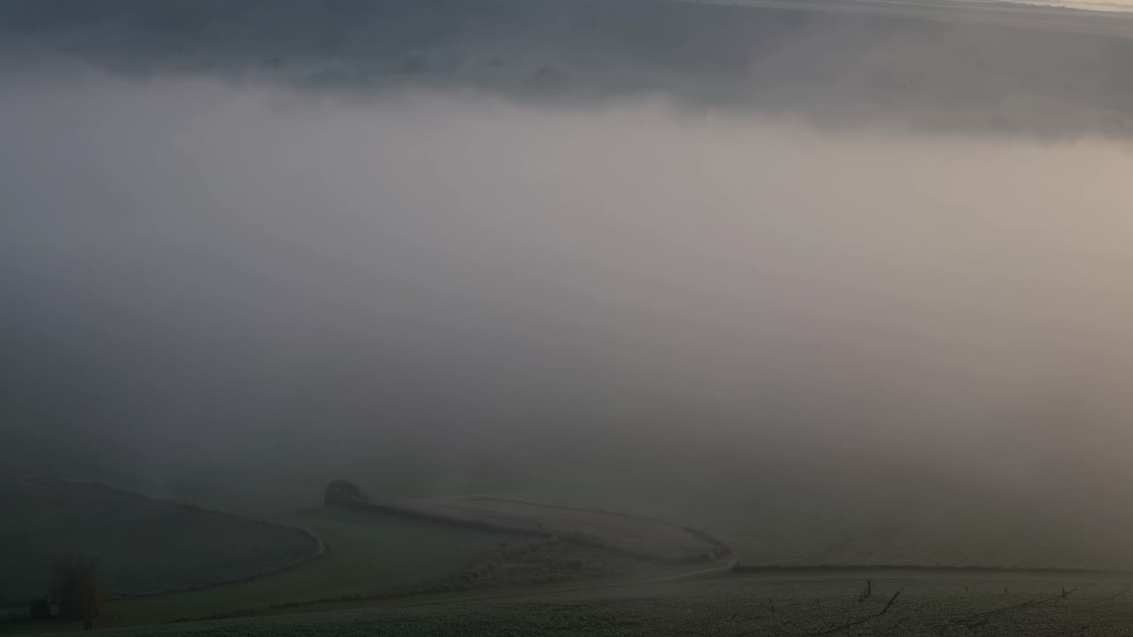 Soft sunlight filters through a thick blanket of fog, creating a serene and ethereal atmosphere over the landscape, evoking a sense of peace and tranquility