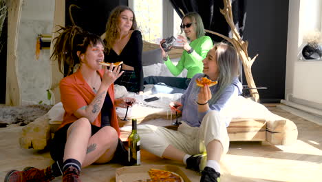 two happy girls eating pizza on the floor while their two friends sitting on the bed and one of them recording with video camera