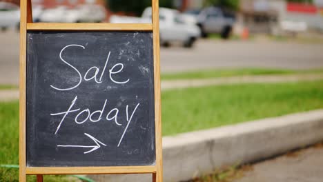 sale today chalkboard and wood a frame sign outside next to green grass and road with cars driving by in the middle of the day, panning side to side