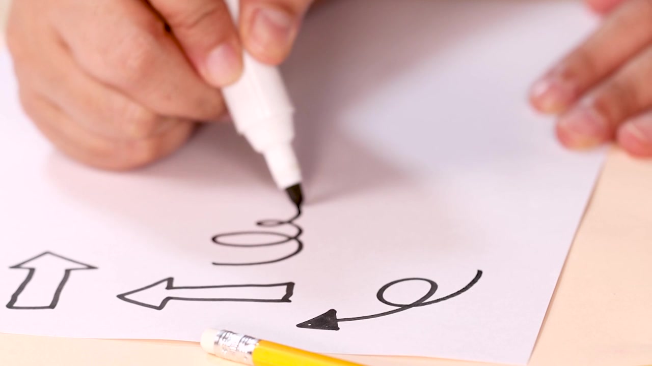 Una persona usa un rotulador negro para dibujar espirales y flechas en papel blanco.
