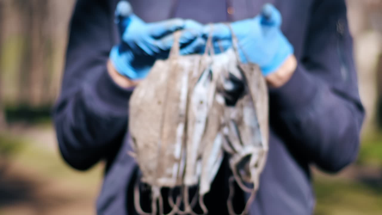 Man in medical gloves holding a bunch of dirty medical masks raised from the ground. Pollution idea