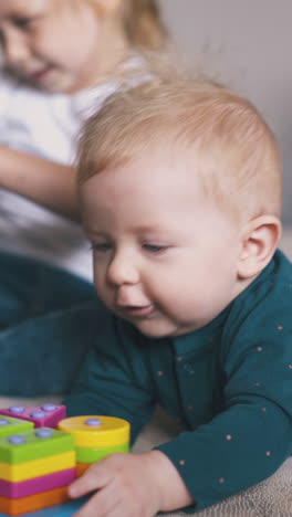 emotional little boy baby plays with colorful plastic toy near blonde sister with pyggybank on large bed at home