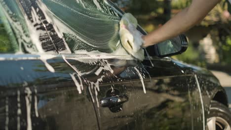 unrecognizable hand of a caucasian man washing a black car with soap and sponge