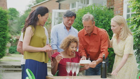 Gruppe-Reifer-Freunde-Bei-Einer-Überraschungs-Geburtstagsfeier-Für-Eine-Frau-Im-Garten-Mit-Kuchen-Und-Champagner