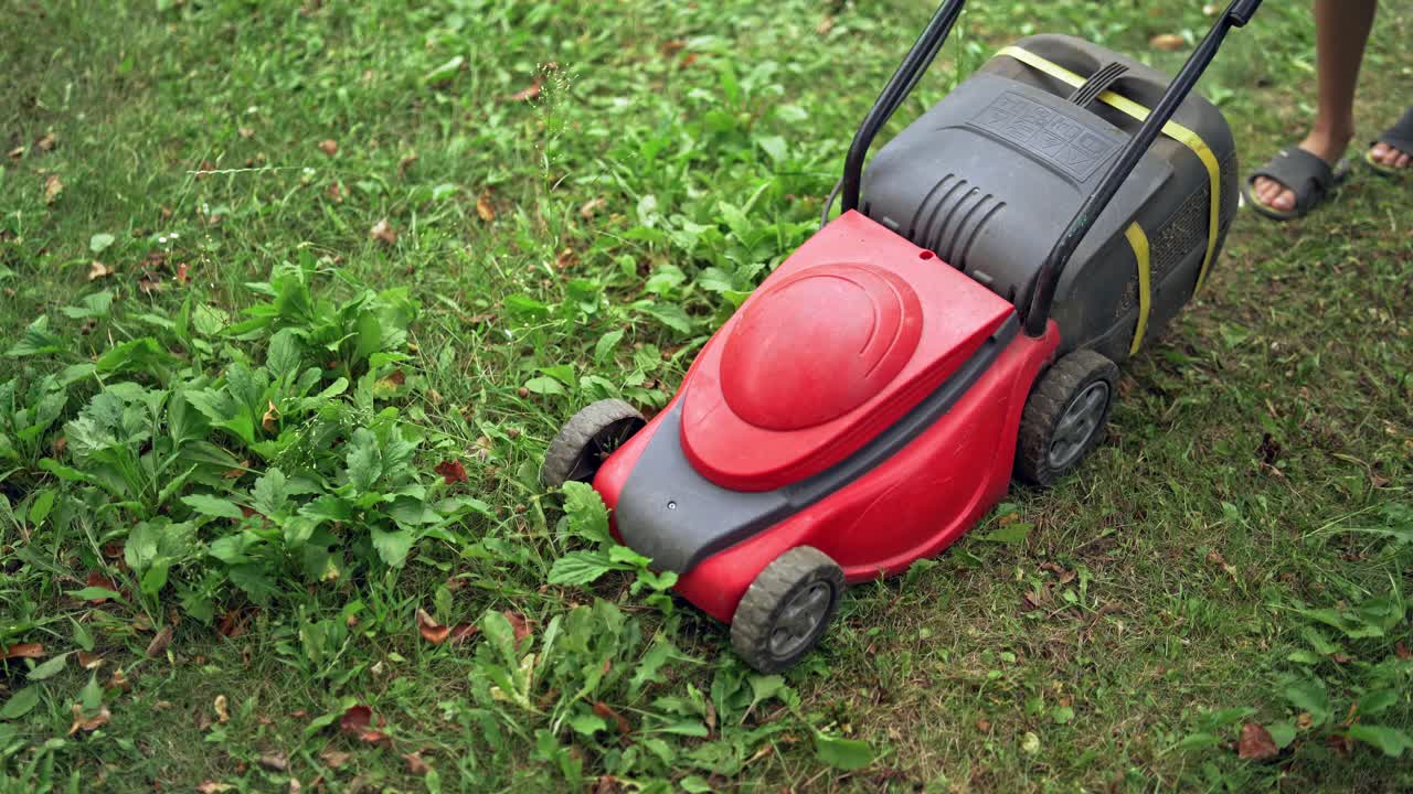 Working process of lawn mower outdoors. Boy cutting grass in his yard with corded electric lawn mower.