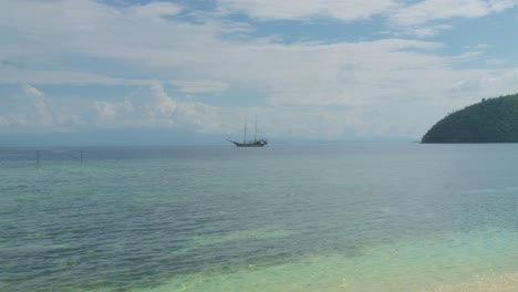 Traditional-sailing-boat-floats-in-a-distance-on-the-turquoise-waters-of-Raja-Ampat,-Indonesia